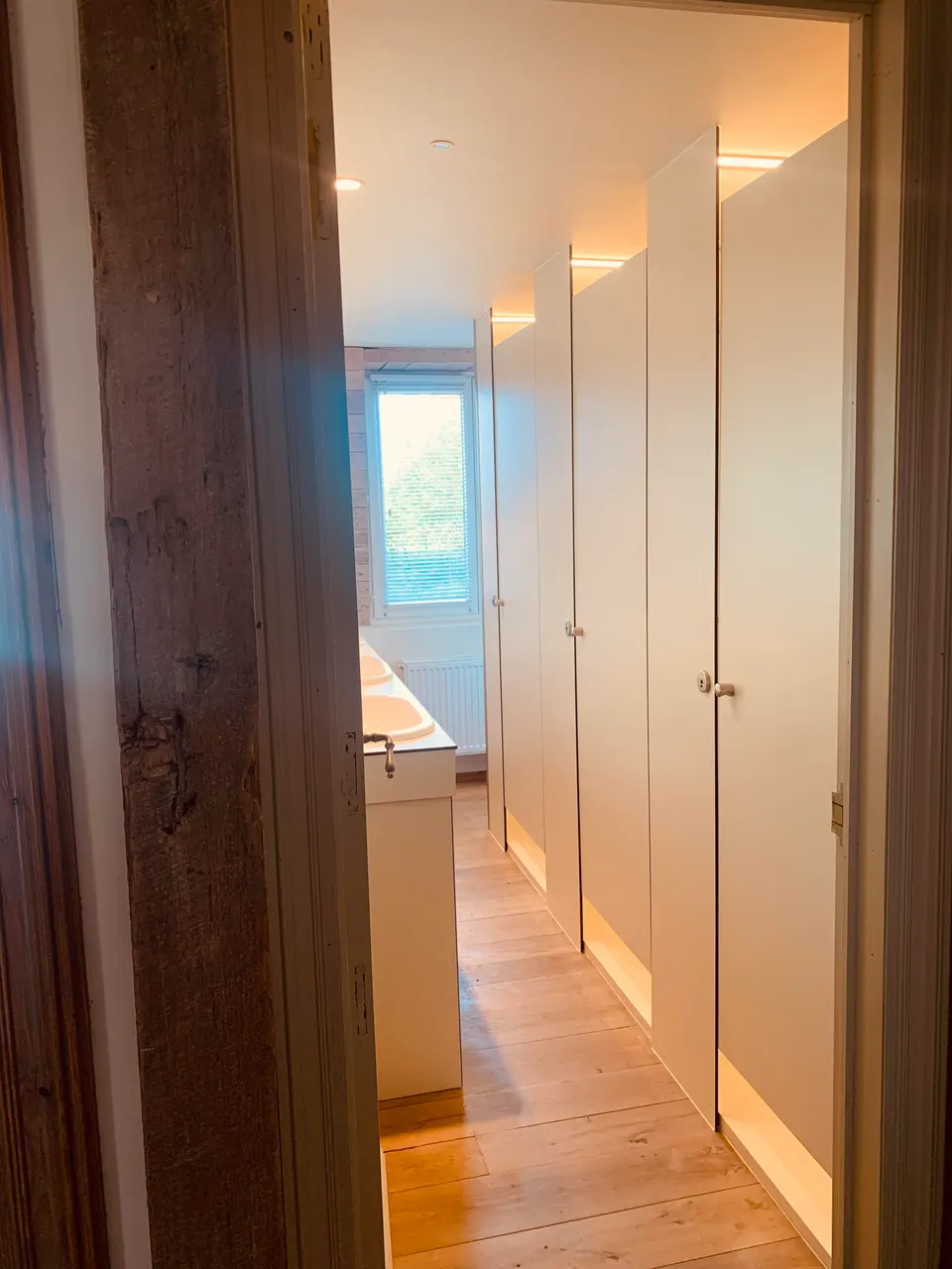 Washroom with a row of white doors, a washbasin and a wooden floor, with a window at the end