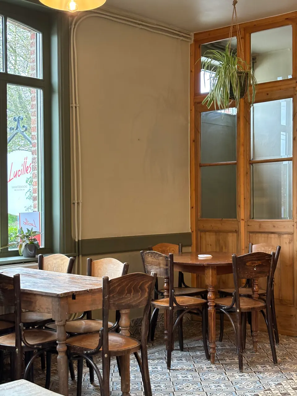 The café with wooden tables and bistro chairs, a tall window and a cement-tile floor
