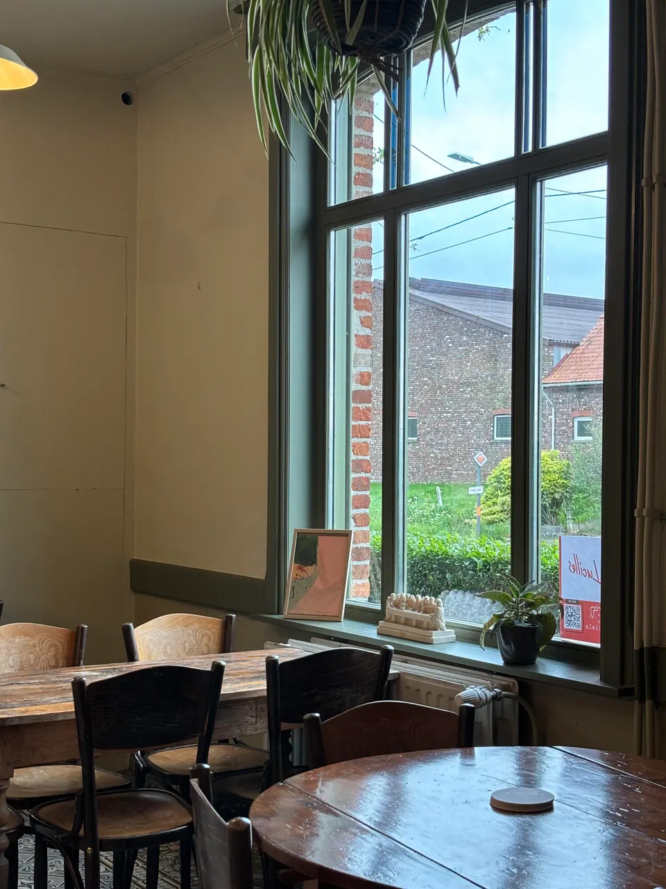 Café tables and chairs by a large window looking out on the street and brick houses