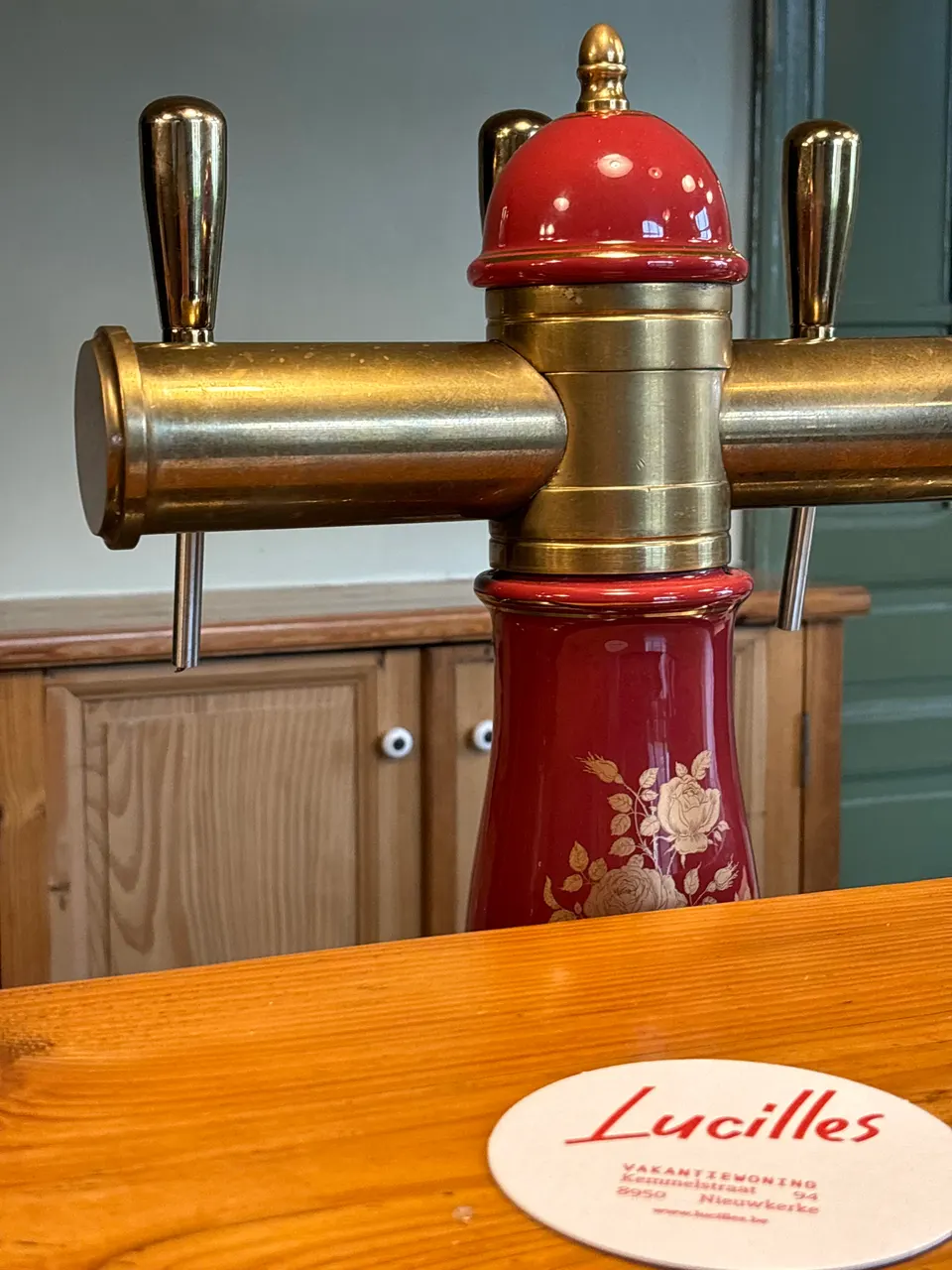 Brass beer tap with a red porcelain column on the wooden bar, next to a Lucilles beer mat
