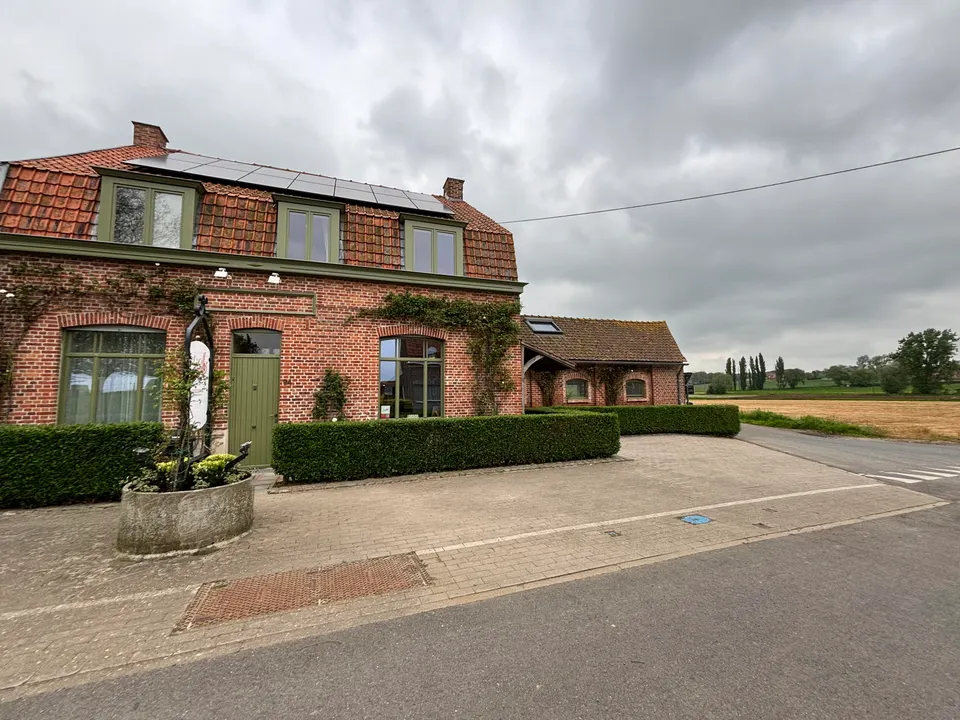 Brick front of Lucilles with green windows and solar panels, a field to the right under a grey sky