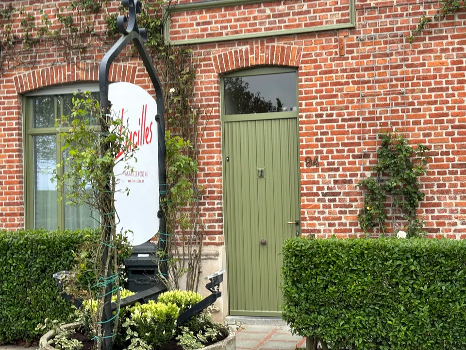 Green front door with house number 94 in a brick facade, beside the Lucilles sign and a hedge
