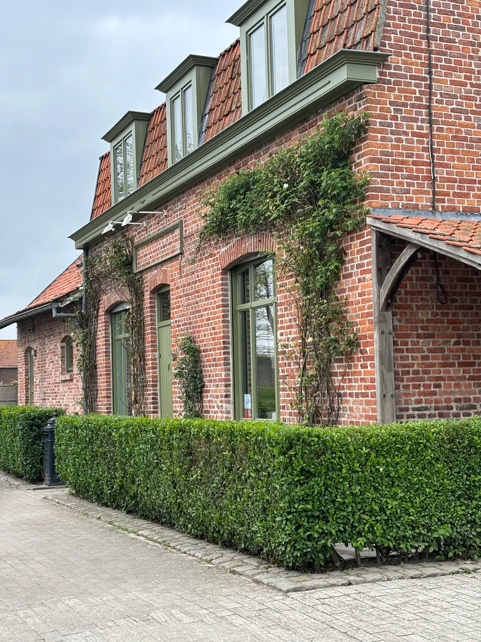 Corner of the brick facade with green dormers, climbing plants and a low hedge