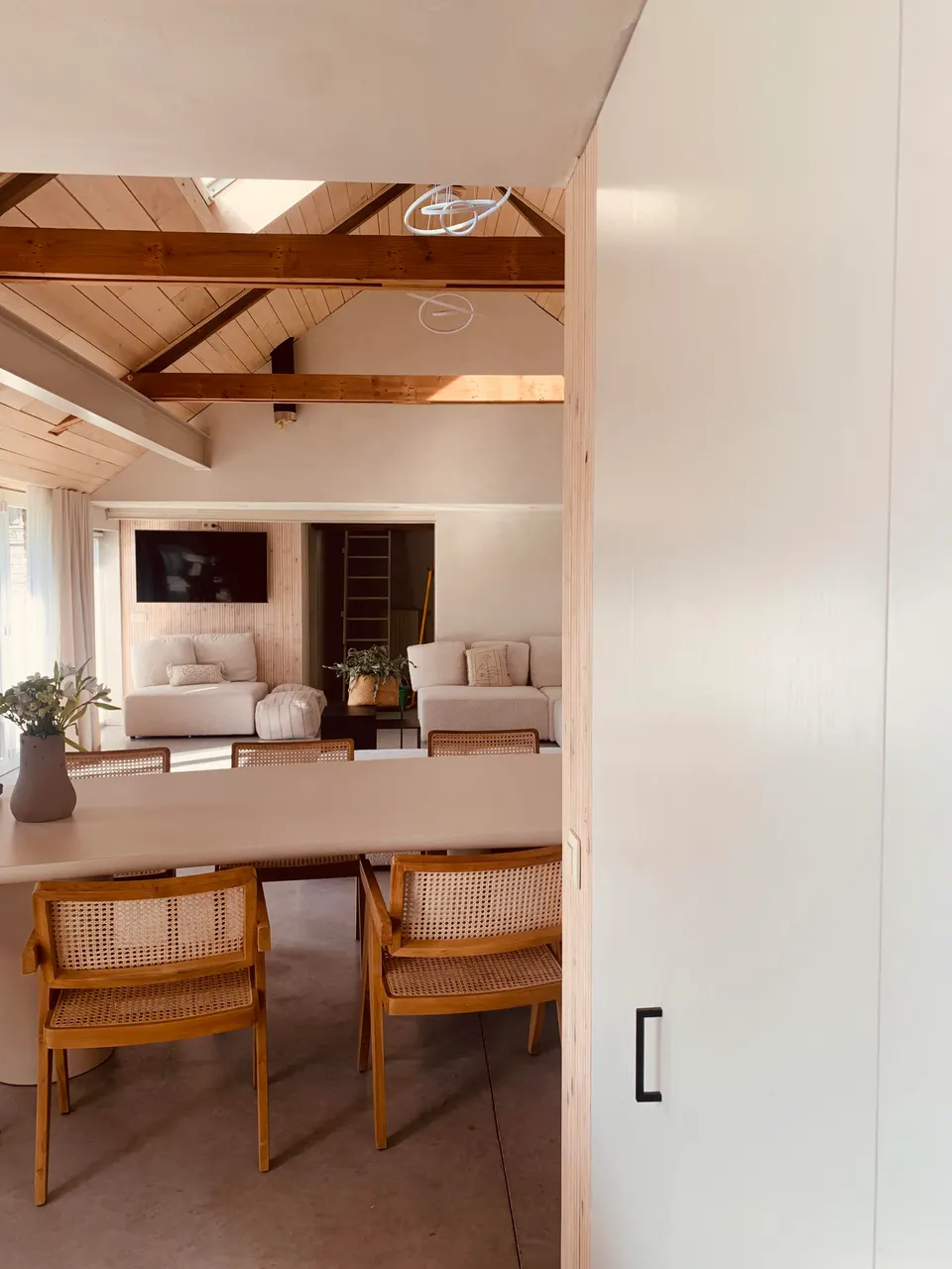 View into the living room: long dining table, cane chairs, sofas and timber roof beams