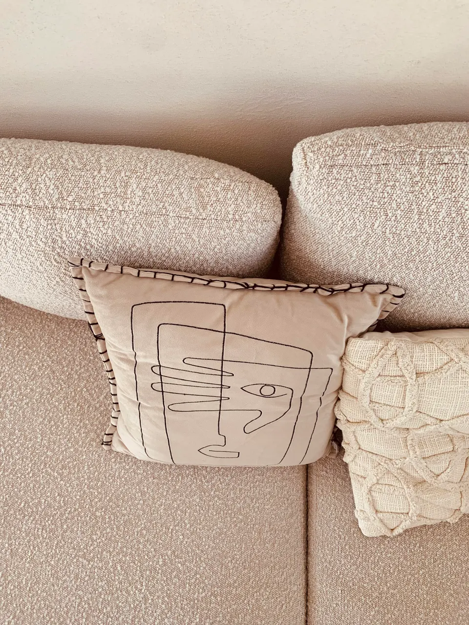 Beige bouclé sofa with a cushion showing a line drawing of a face