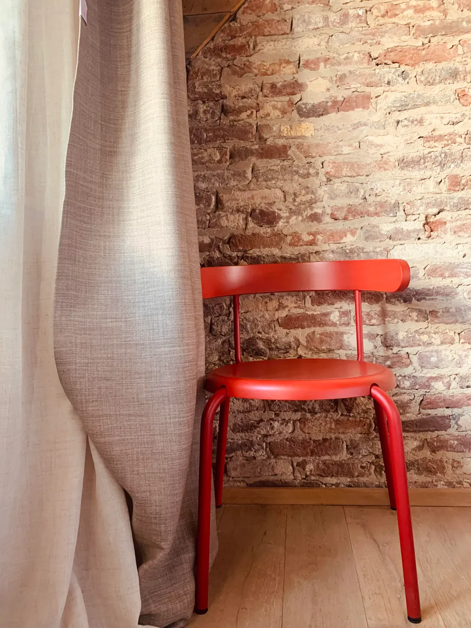 Red chair against a brick wall next to a linen curtain