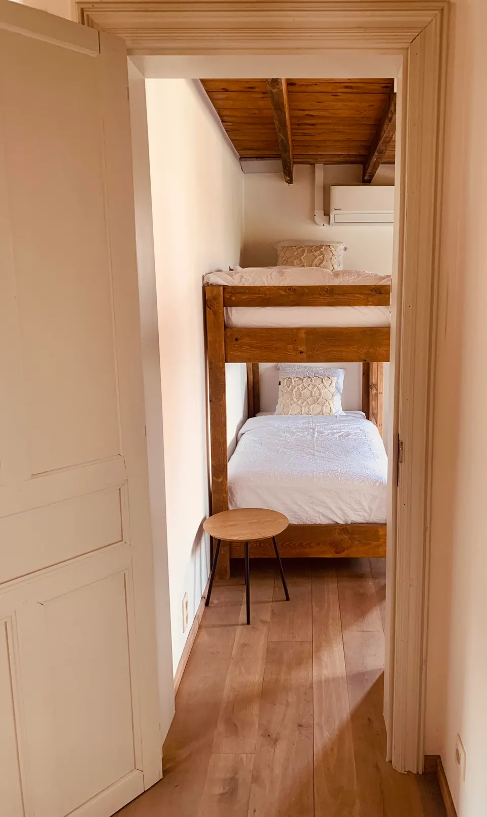 View into a small bedroom with a wooden bunk bed, a stool and a wooden floor