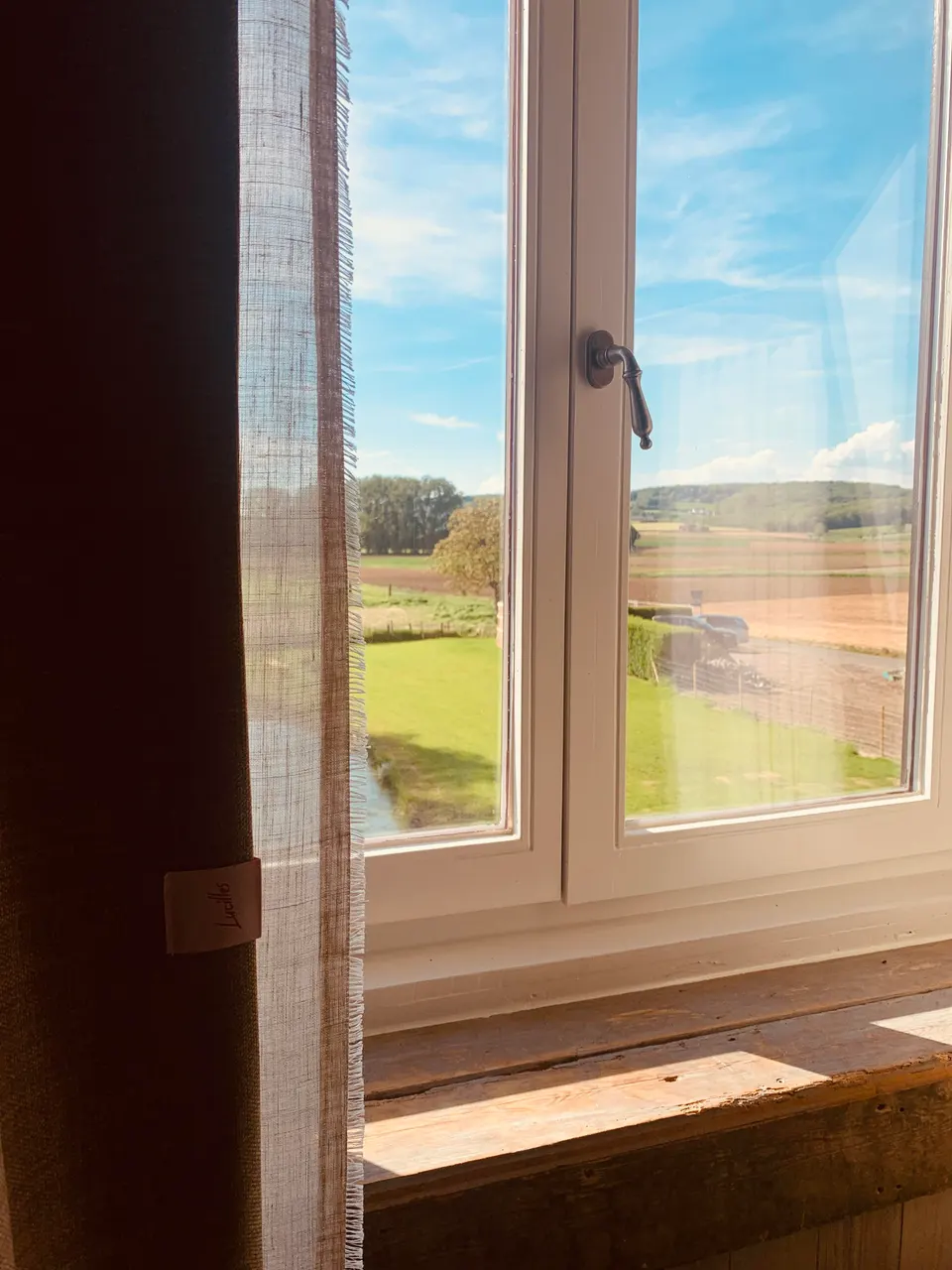 Open window with a linen curtain, looking out over the garden, fields and rolling hills