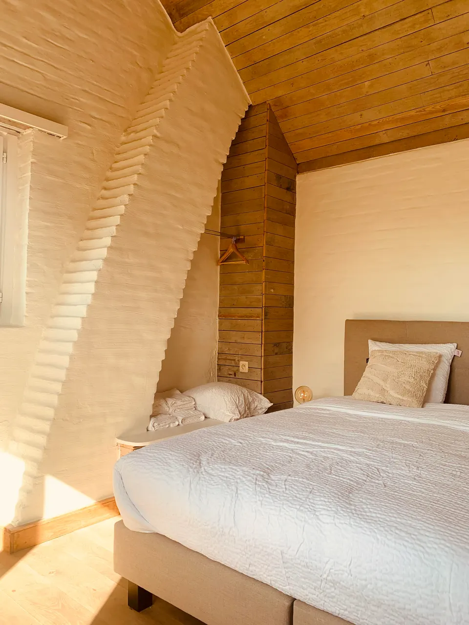 Sunny attic bedroom with a sloping wall, wooden ceiling and a double bed with white bedding