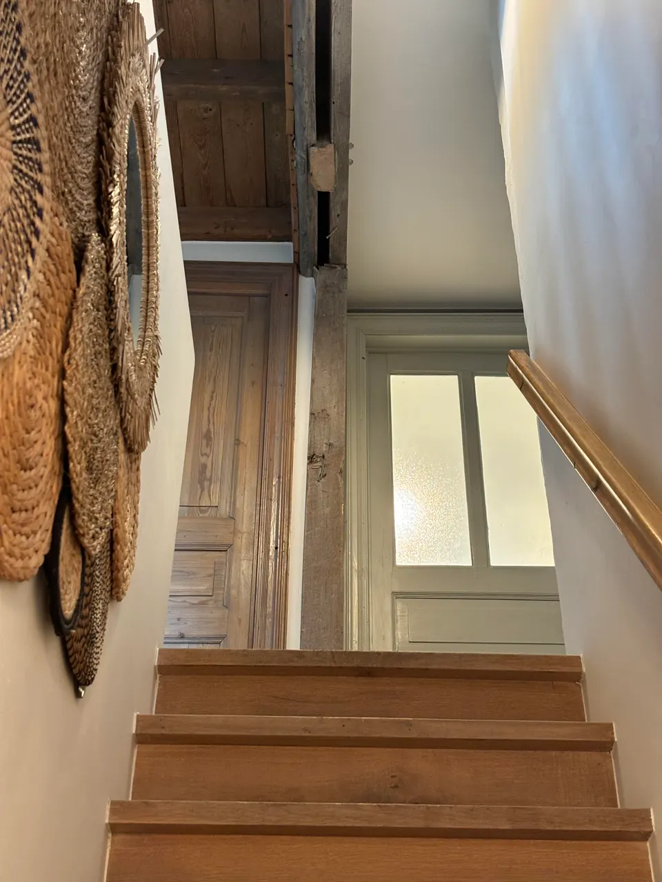 Wooden staircase with a handrail and woven wall decorations, a frosted-glass door at the top