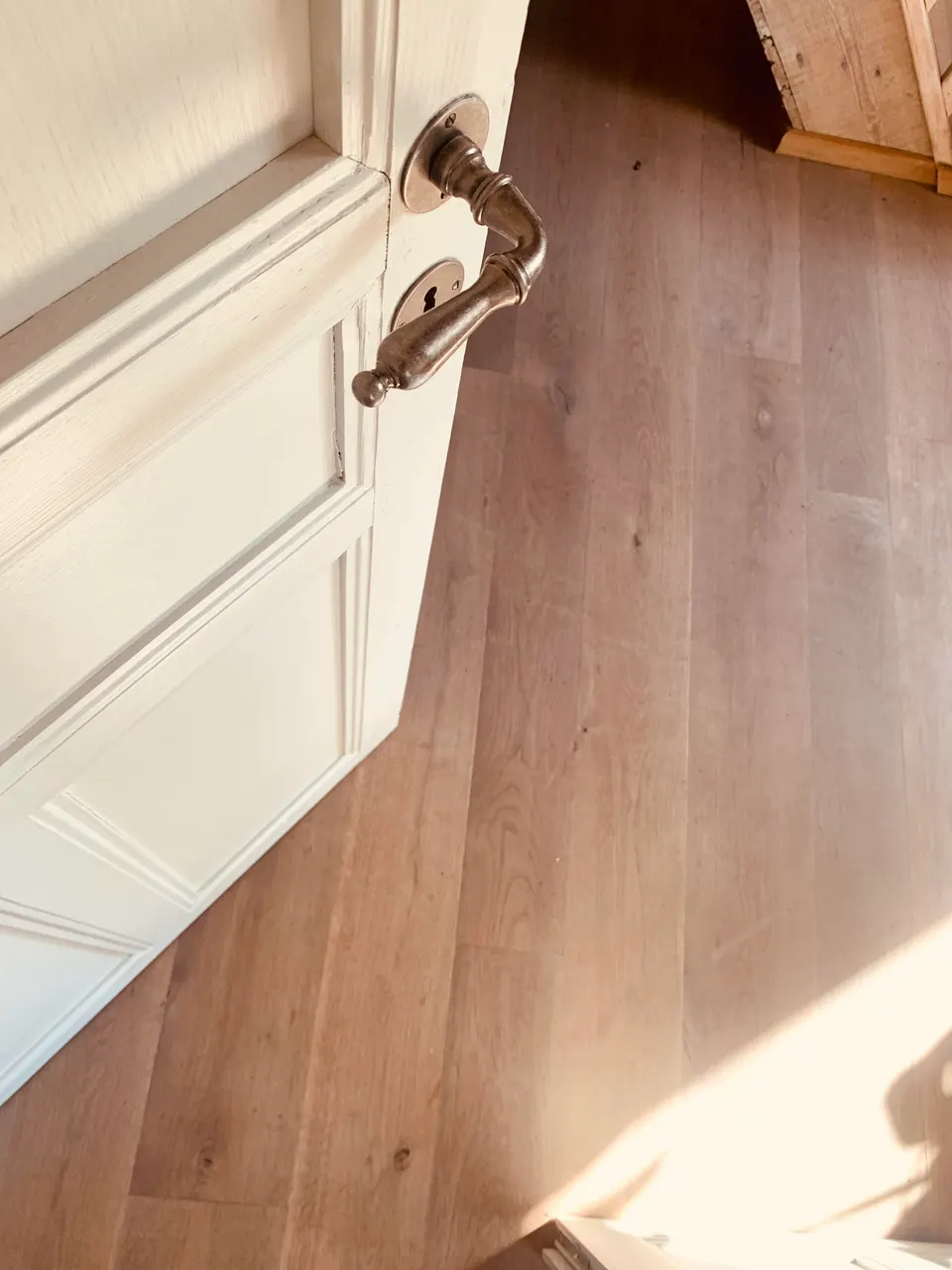 Old white panelled door with a brass handle, half open onto a wooden plank floor