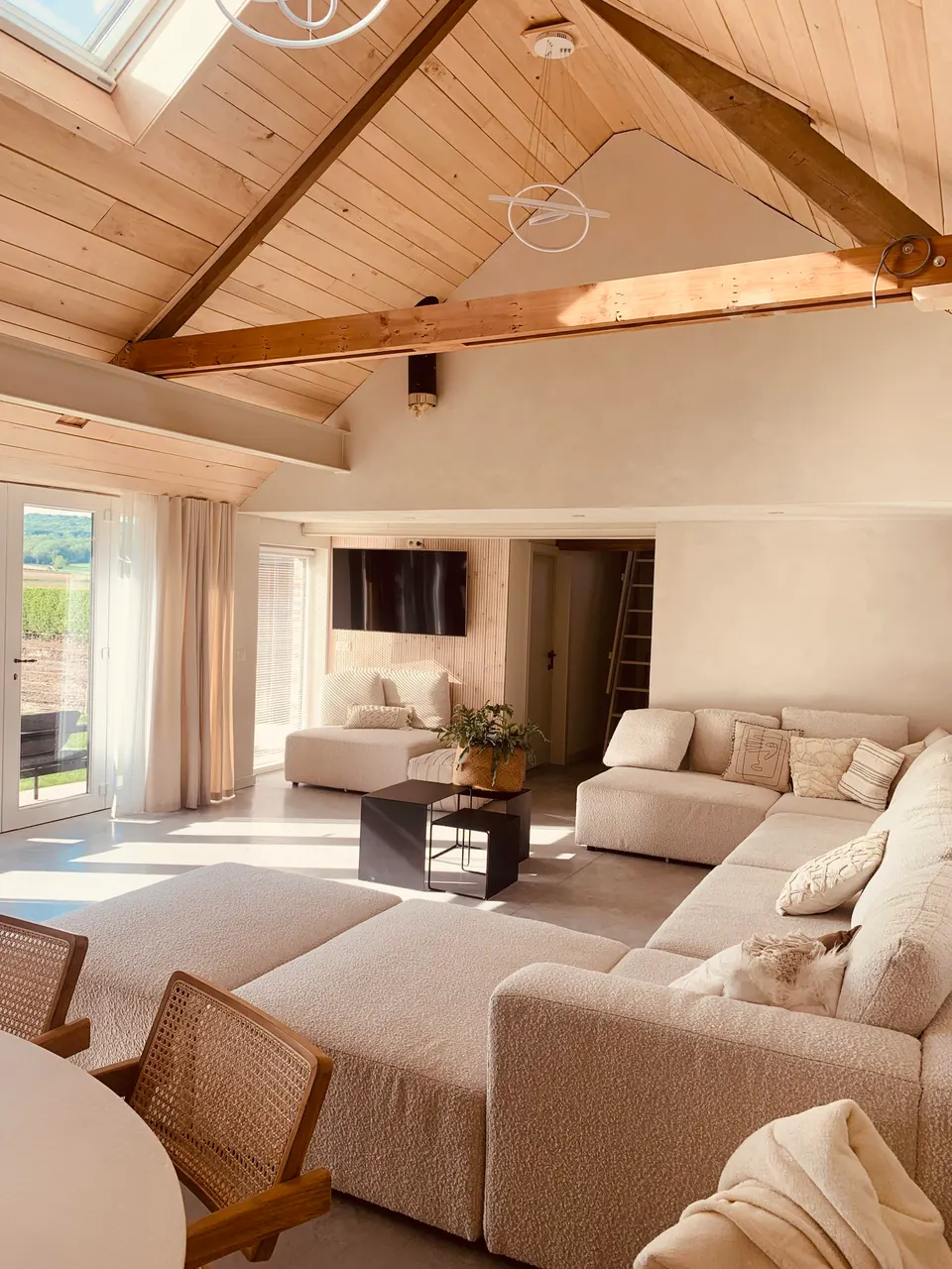 Living room under a timber roof with a large beige corner sofa, coffee tables and a view outside