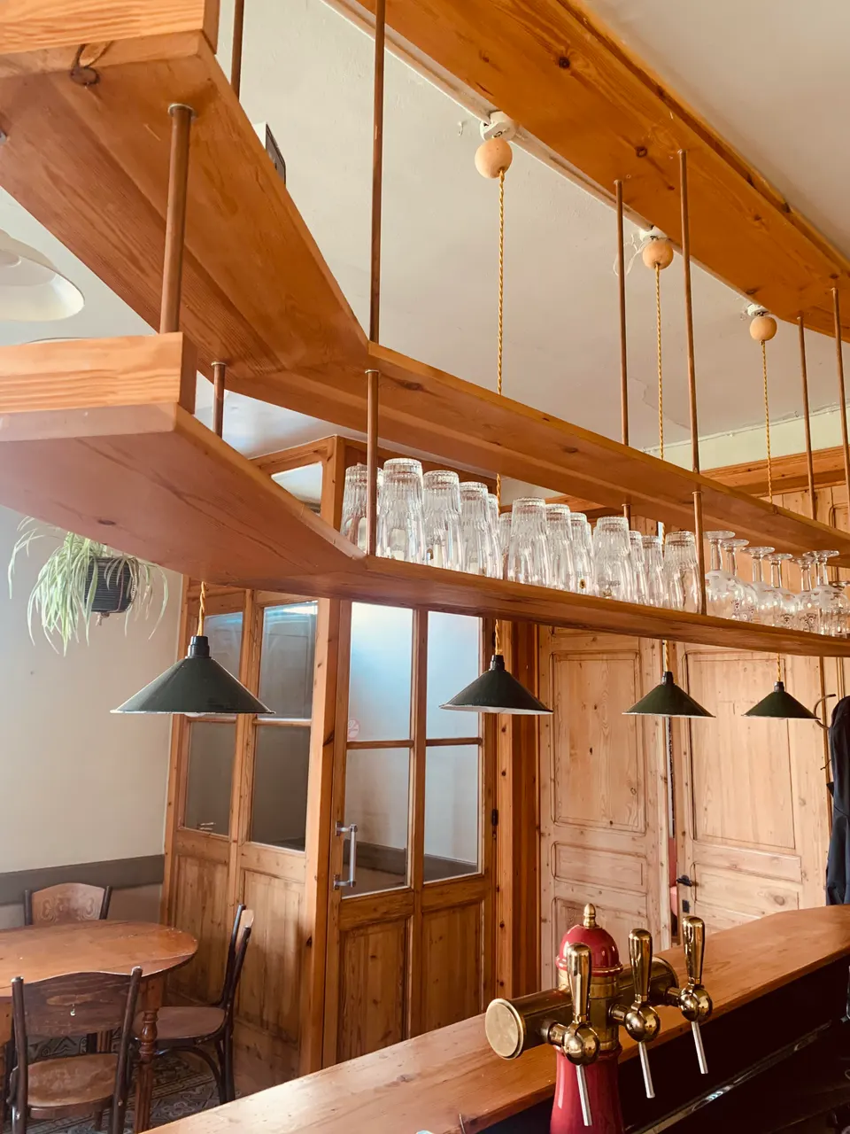 Hanging wooden rack full of glasses above the bar and beer taps, with wooden glazed doors behind