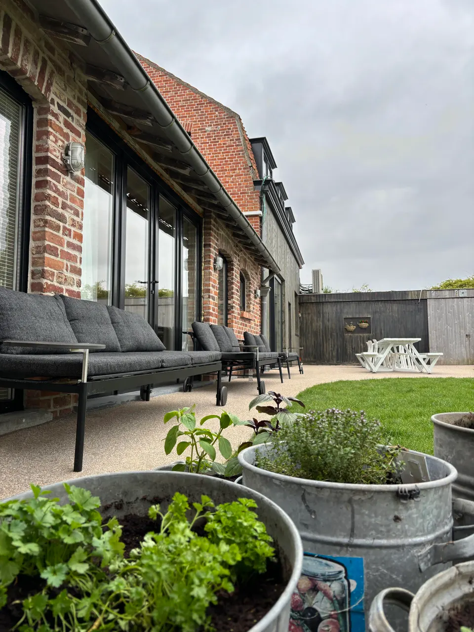 Terrace along the brick rear wall with lounge sofas, zinc tubs of herbs and a white picnic table