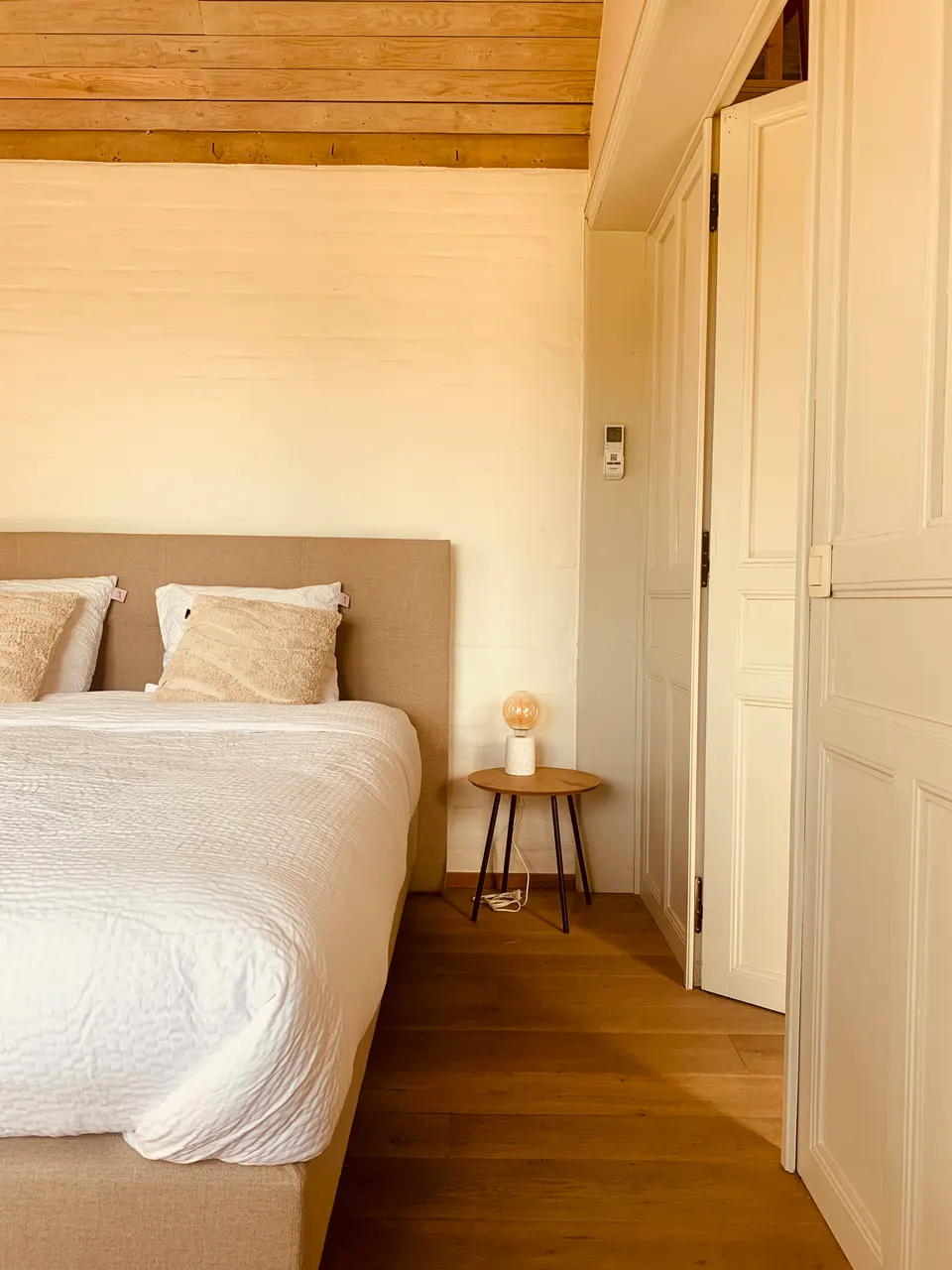Bedroom with a double bed, beige headboard, white bedding and a bedside table with a lamp