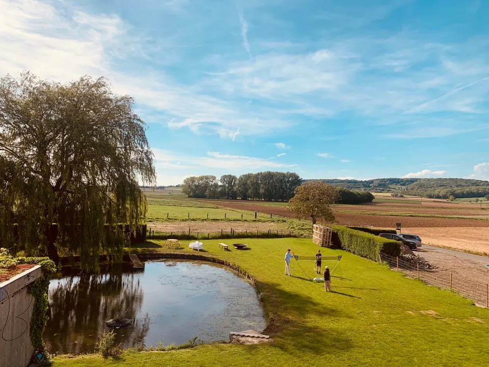 Le jardin vu d’en haut : étang et saule pleureur, pelouse avec filet de badminton, champs jusqu’aux collines