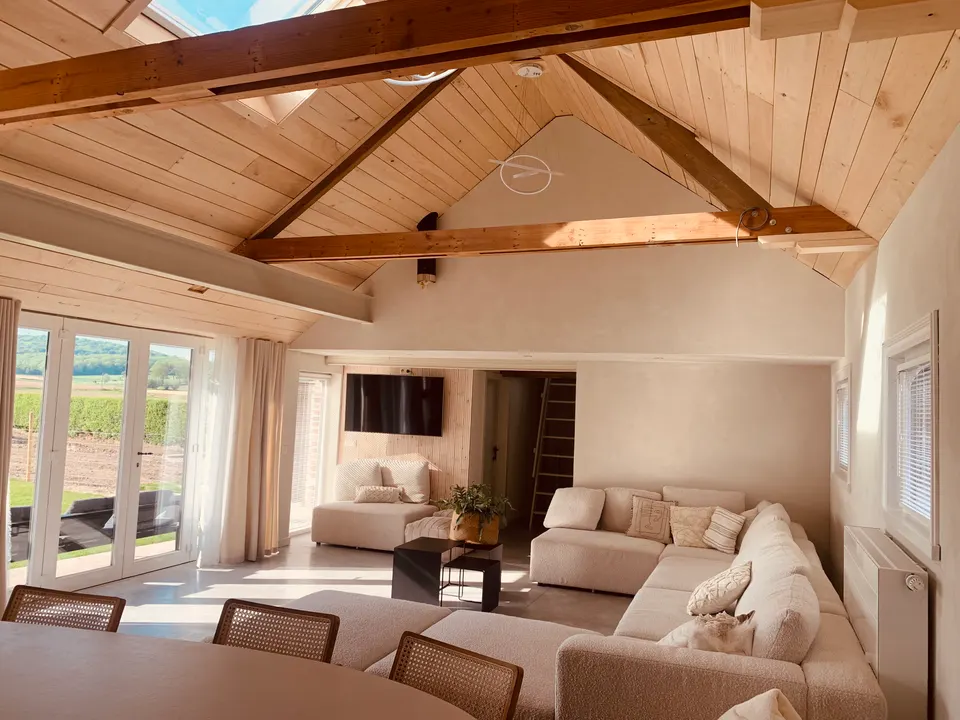 Bright living room under exposed timber beams, a large corner sofa, dining table and glass doors to the garden