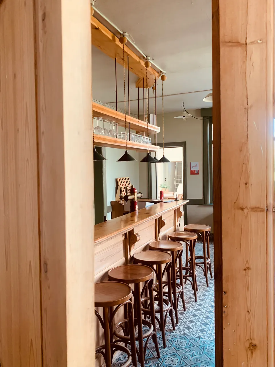 Comptoir en bois et tabourets dans le café, des verres sur une étagère suspendue, sol en carreaux de ciment bleus
