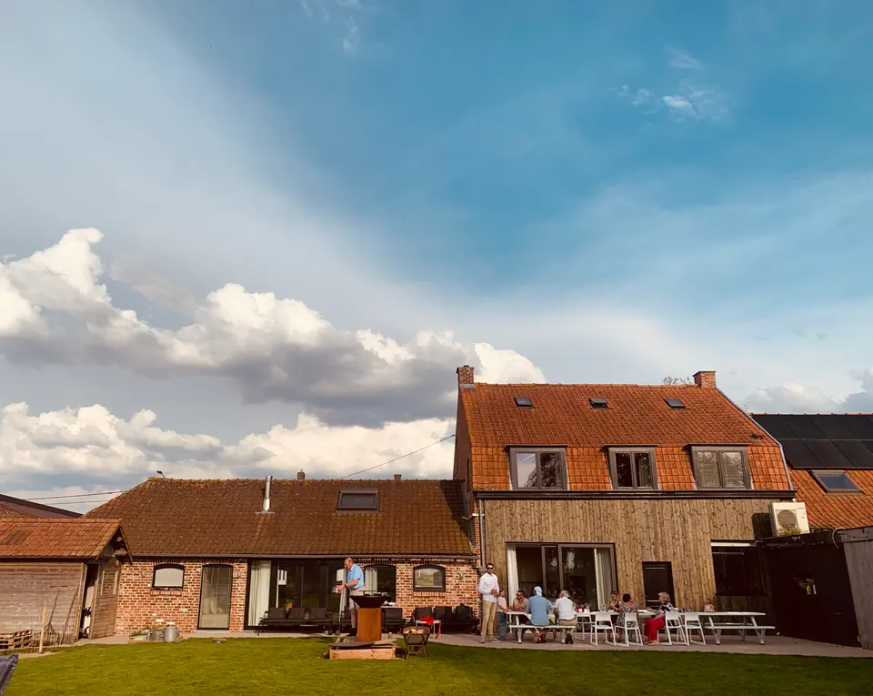 L’arrière de la maison sous un ciel bleu nuageux, avec un groupe d’hôtes sur la terrasse