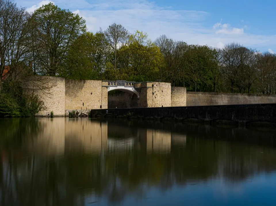 Old ramparts with an arched gateway, reflected in the water of the moat